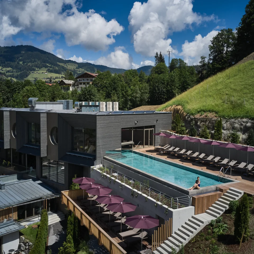 Sporthotel Wagrain mit Pool auf Dachterrasse, Liegen und Blick auf grüne Hügel unter blauem Himmel