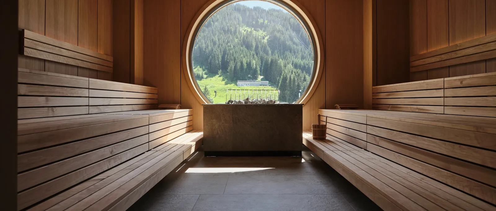 Wooden sauna with round window view of green mountain landscape