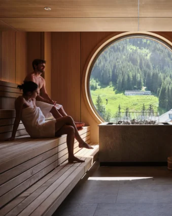 Sauna with two people in front of a round window overlooking a green landscape