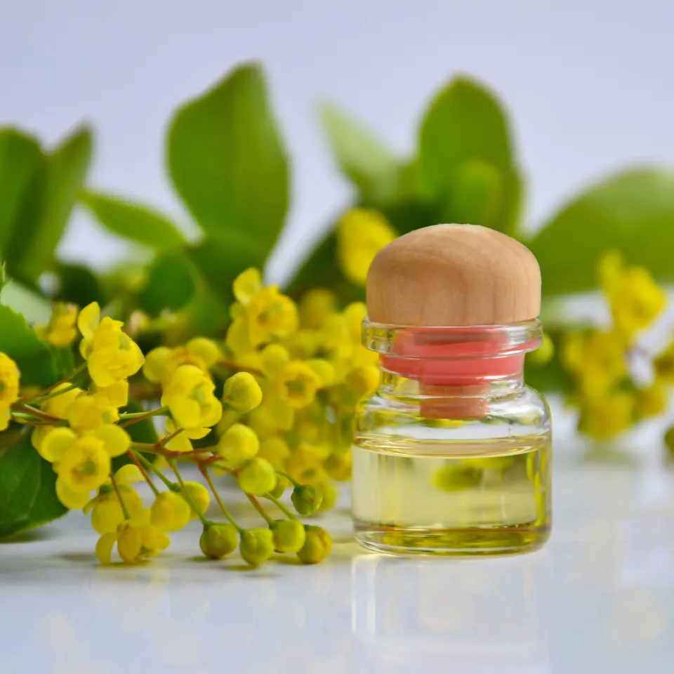 Massageöl in Glasflasche mit Holzdeckel neben gelben Blüten und grünen Blättern