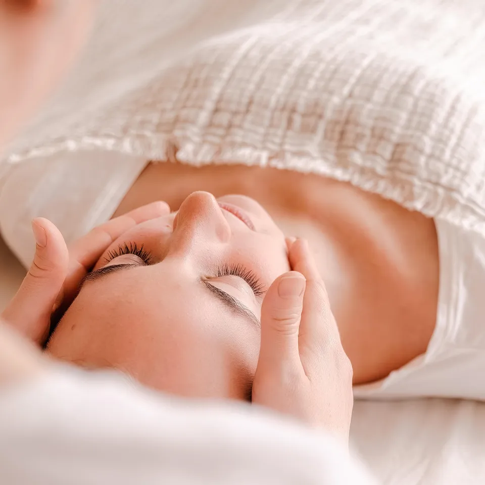 Frau liegt entspannt, Hände berühren sanft ihr Gesicht bei einer Massage