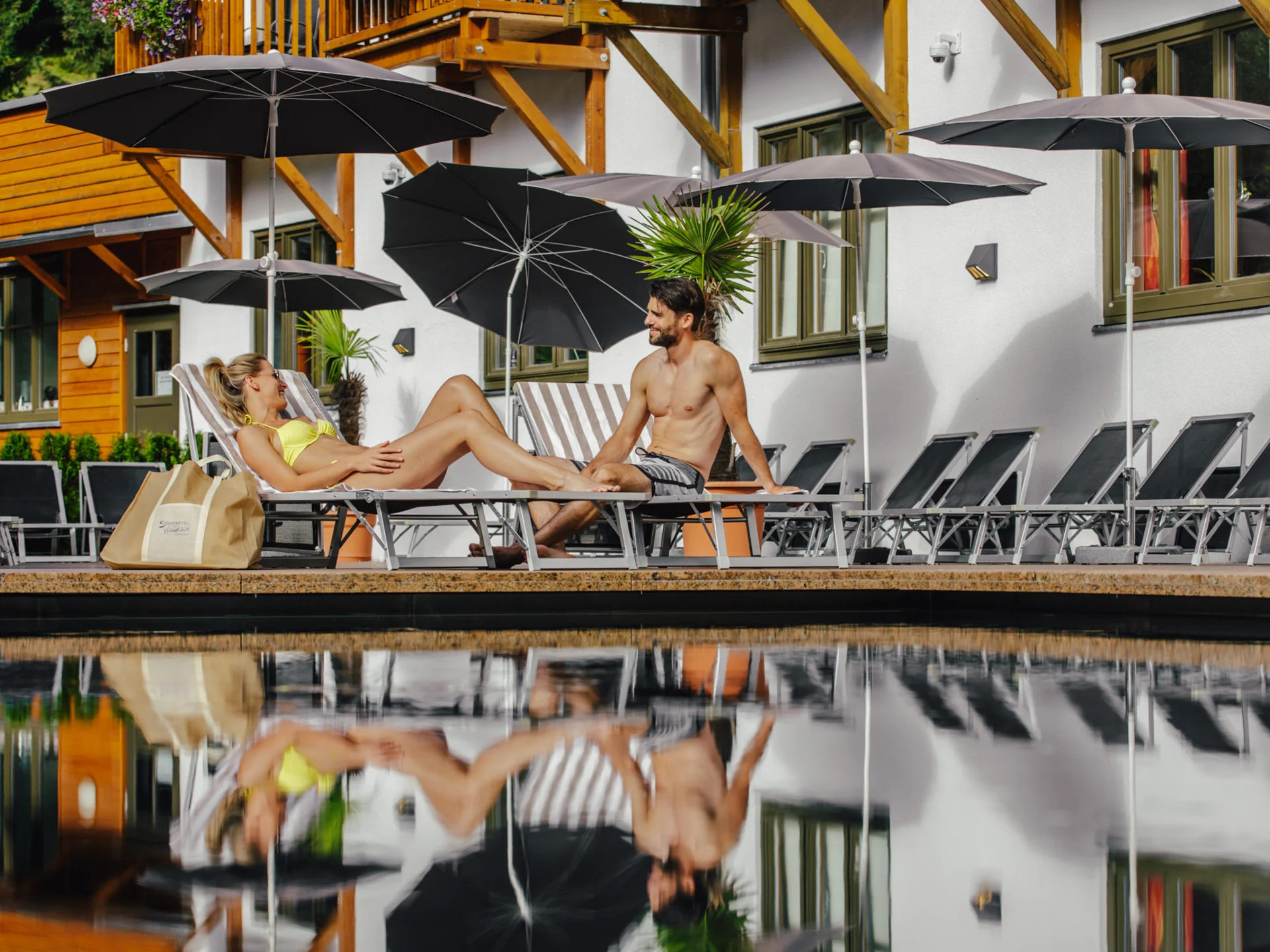 Paar entspannt am Außenpool eines Hotels unter Sonnenschirmen