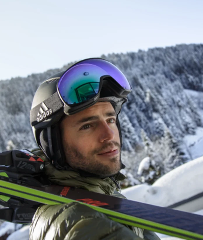 Mann mit Skihelm und Skibrille vor verschneiter Berglandschaft