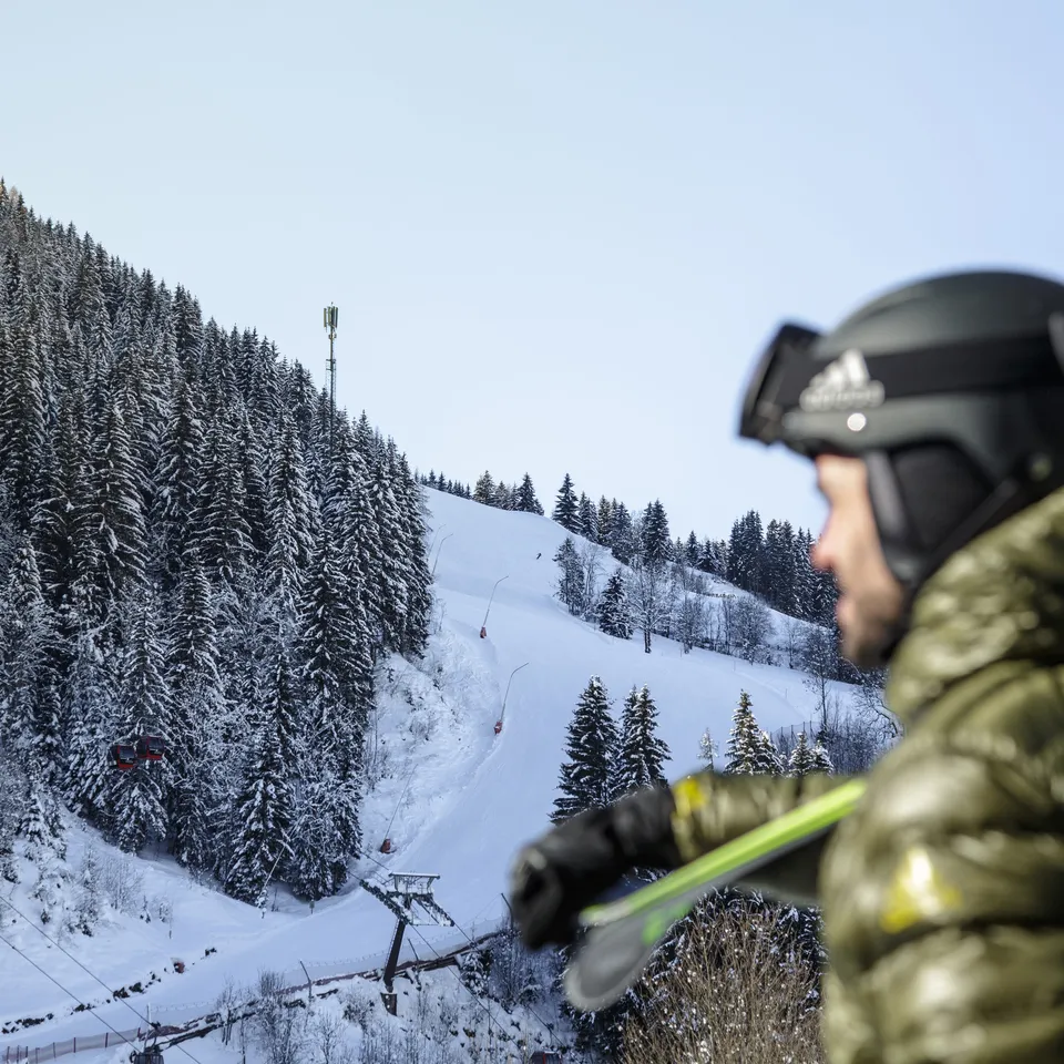 Skifahrer mit Helm blickt auf verschneiten Hang mit Lift und Wald