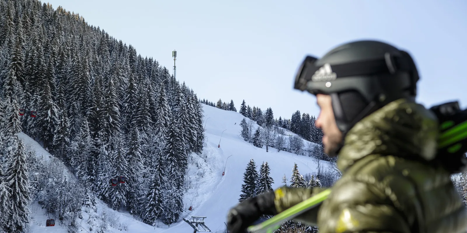 Skier with helmet looks at snowy slope with lift and forest