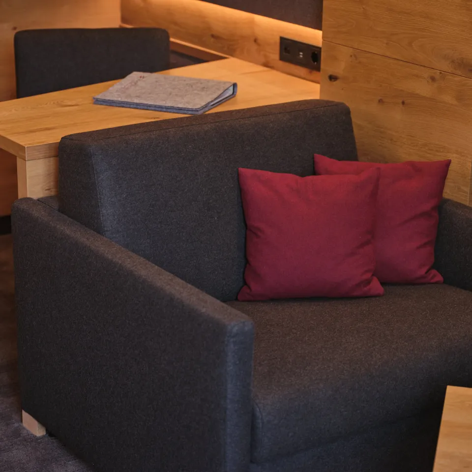 Dark grey armchair with two red cushions in front of wooden wall and desk