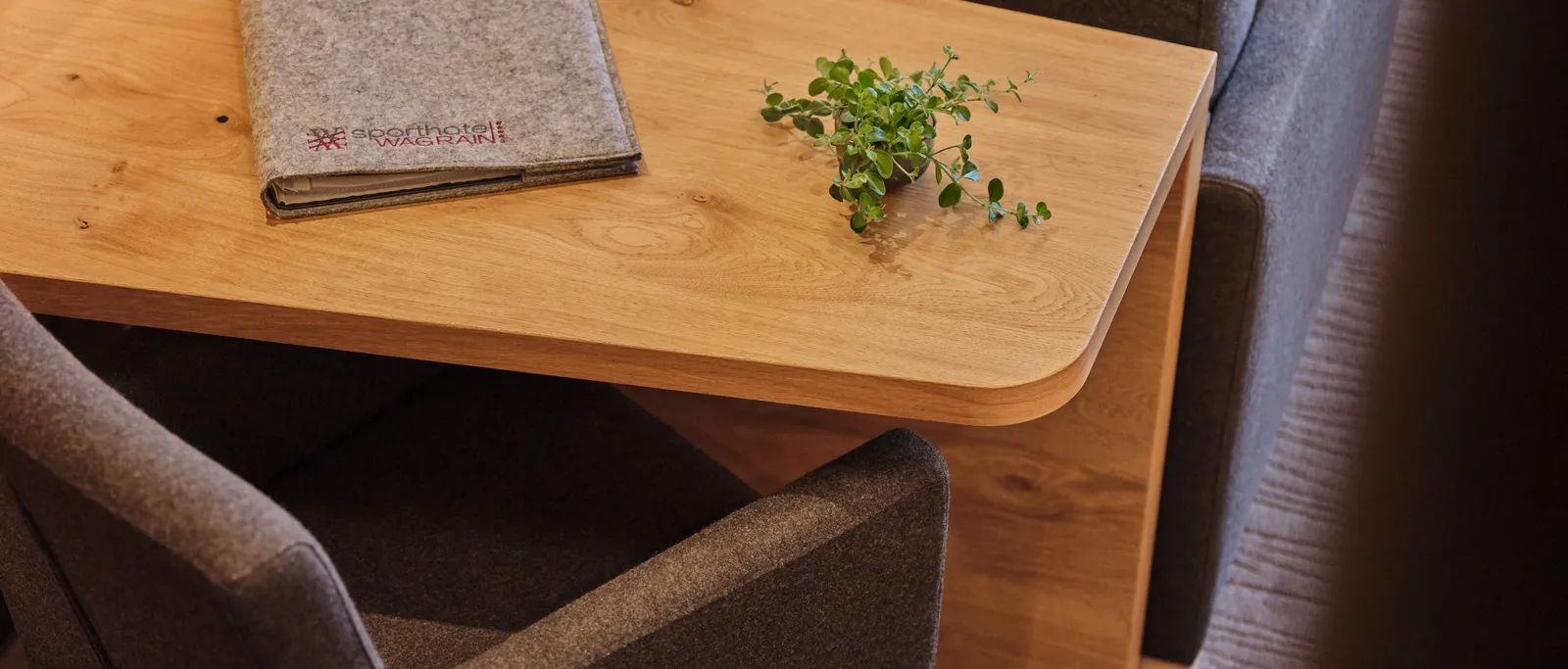 Holztisch mit Filzunterlage und Pflanze zwischen grauen Sesseln