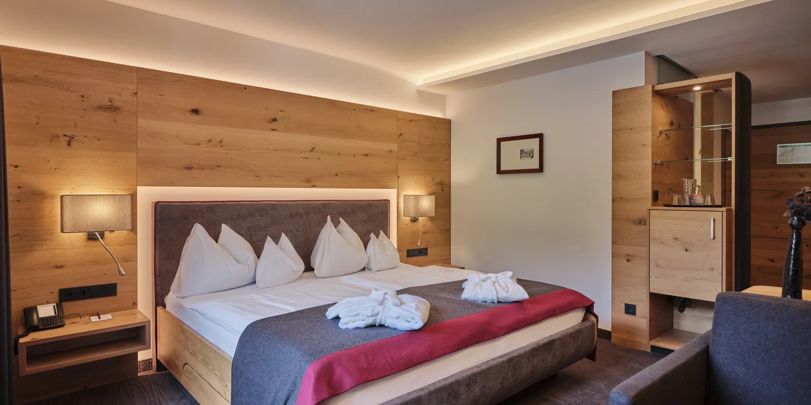 Hotelzimmer mit Doppelbett, Holzwand und indirekter Beleuchtung