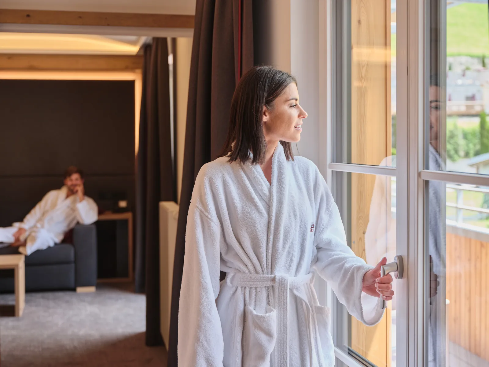 Frau im Bademantel öffnet Fenster in Hotelzimmer