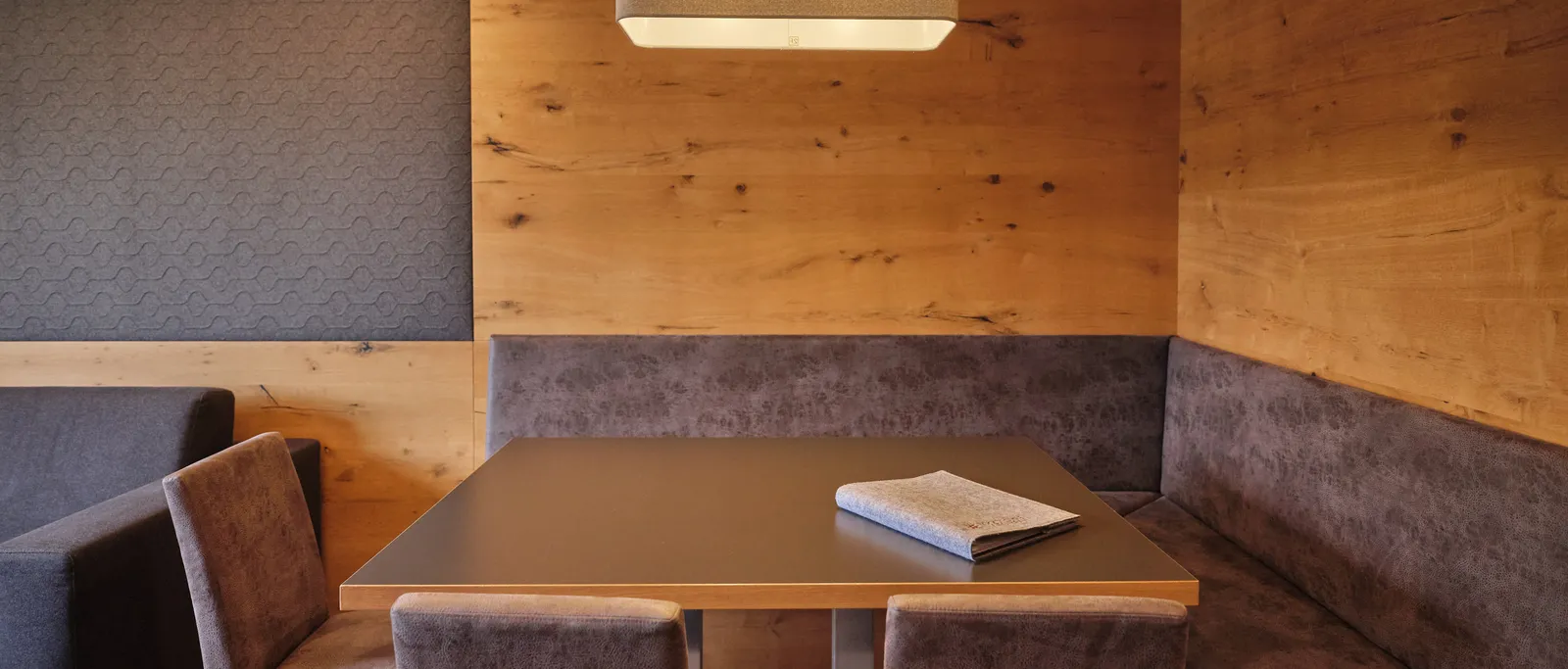 Dining area with wooden wall, table, chairs, corner bench and a rectangular lamp