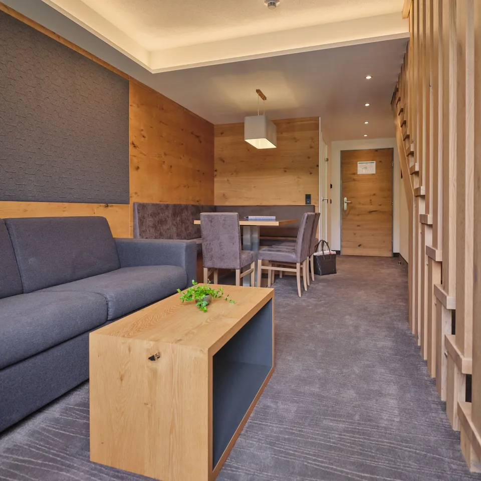 Hotelzimmer mit Sofa, Tisch, Stühlen und Holzelementen