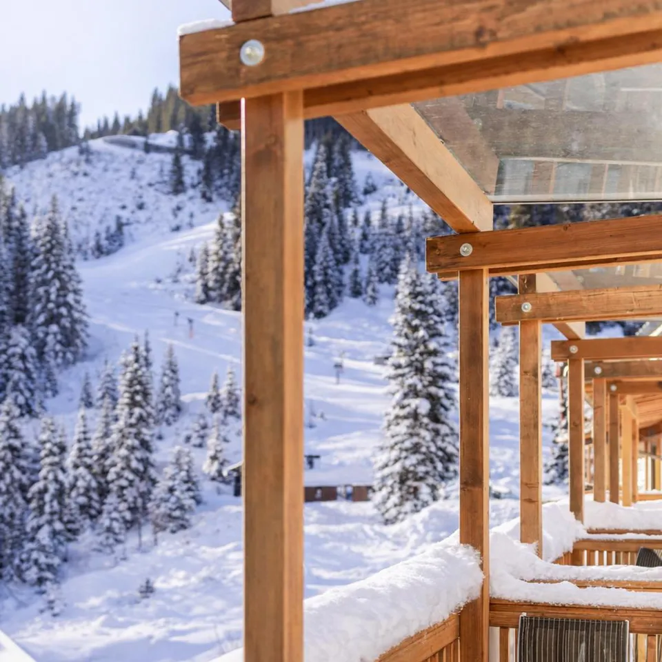 Snow-covered wooden terrace with mountain view and ski slope