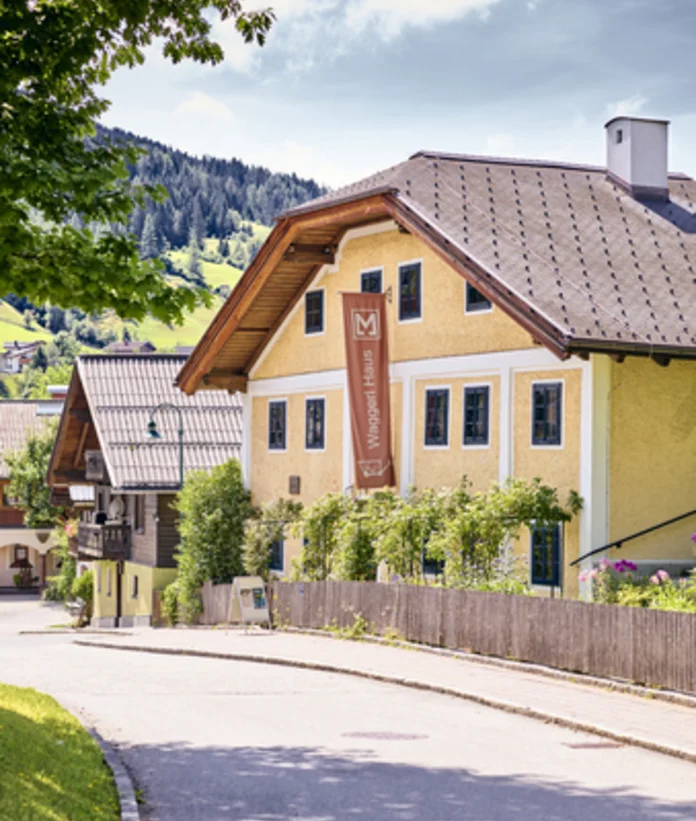 Yellow Waggerl Haus Museum in Wagrain with brown sign and wooden fence on a street