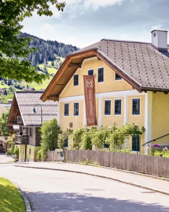 Yellow Waggerl Haus Museum in Wagrain with brown sign and wooden fence on a street