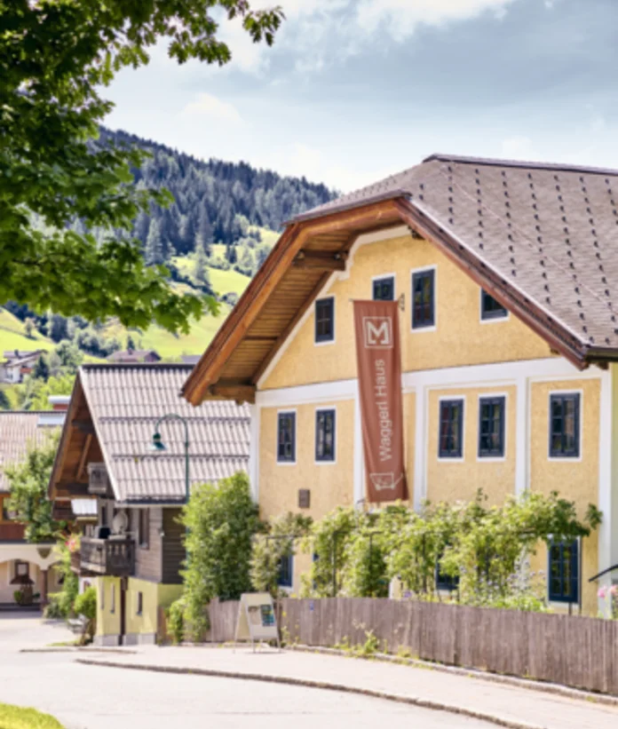 Gelbes Waggerl Haus Museum in Wagrain mit braunem Schild und Holzzaun an einer Straße