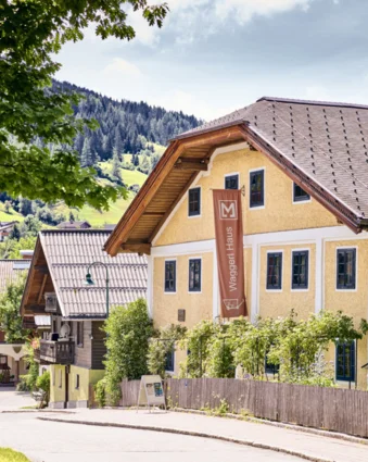 Yellow Waggerl Haus Museum in Wagrain with brown sign and wooden fence on a street