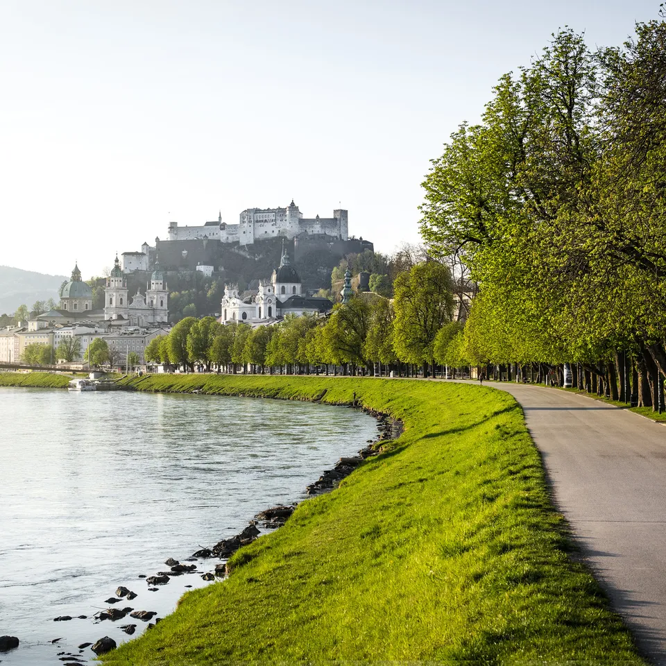 Salzburg with Hohensalzburg Fortress above the Salzach River, riverside path and trees in the foreground