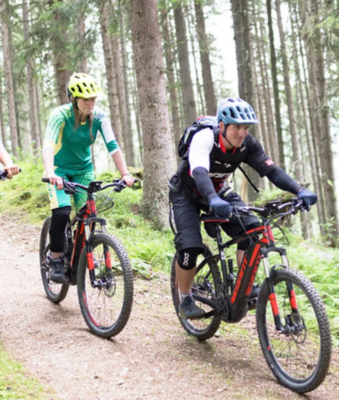 Three mountain bikers ride downhill on a forest path