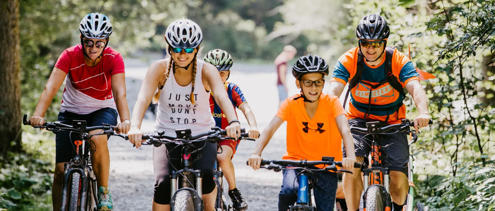 Family with helmets rides on e-bikes along a gravel path in the countryside
