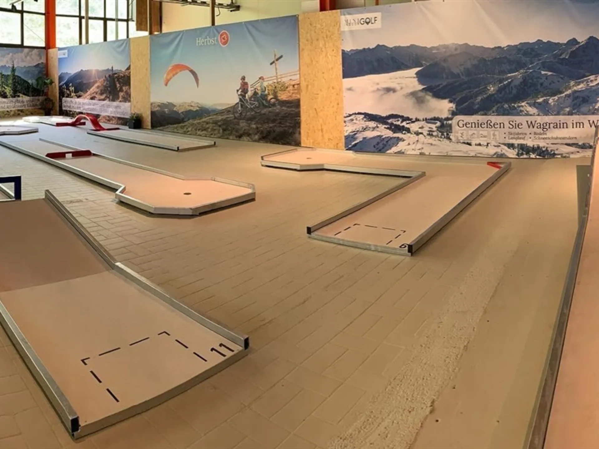 Indoor-Minigolfanlage mit mehreren Bahnen vor Bergpanorama-Hintergrund