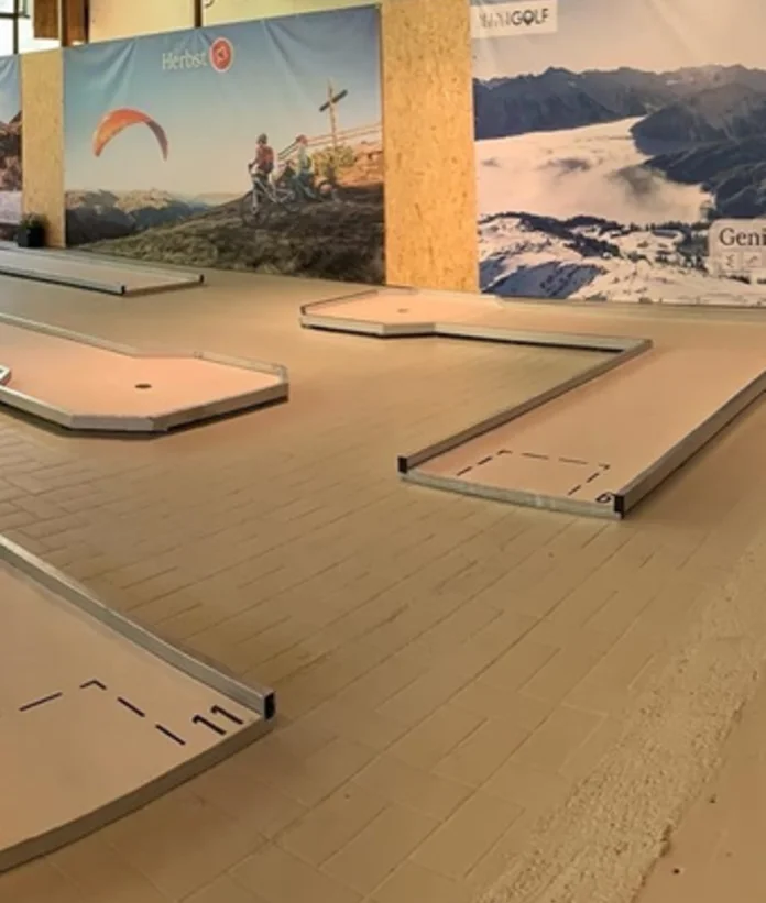 Indoor-Minigolfanlage mit mehreren Bahnen vor Bergpanorama-Hintergrund