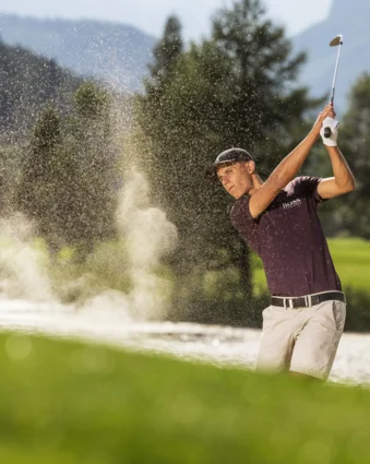 Golfer schlägt Ball aus Sandbunker vor grüner Landschaft