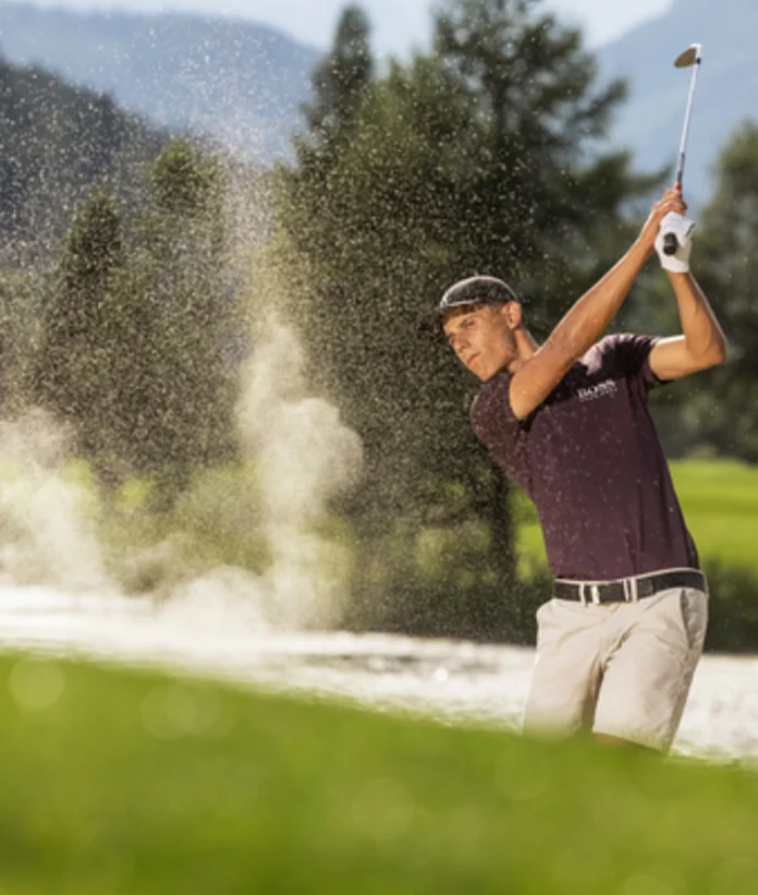 Golfer schlägt Ball aus Sandbunker vor grüner Landschaft