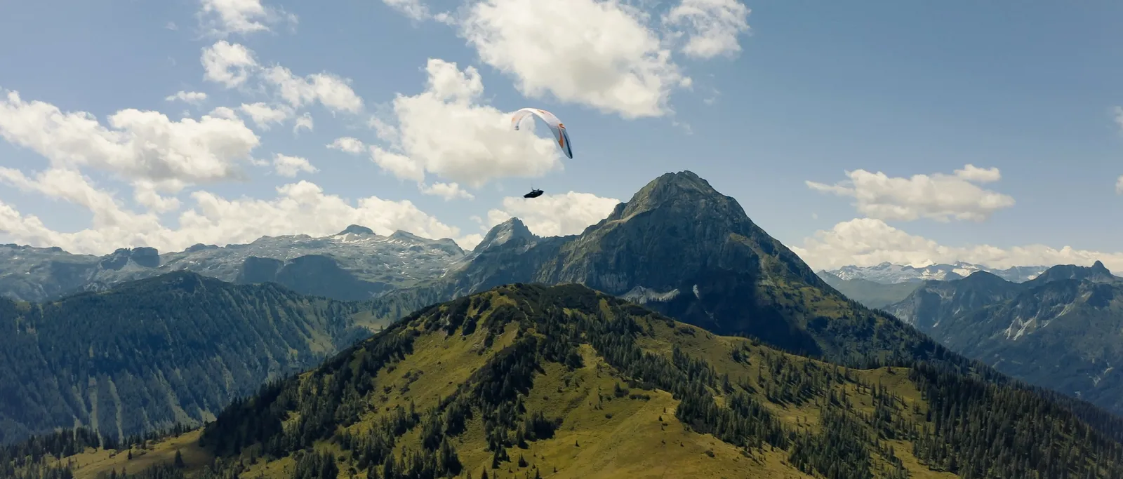 Paragleiter vor Berglandschaft mit grünen Hügeln und bewölktem Himmel