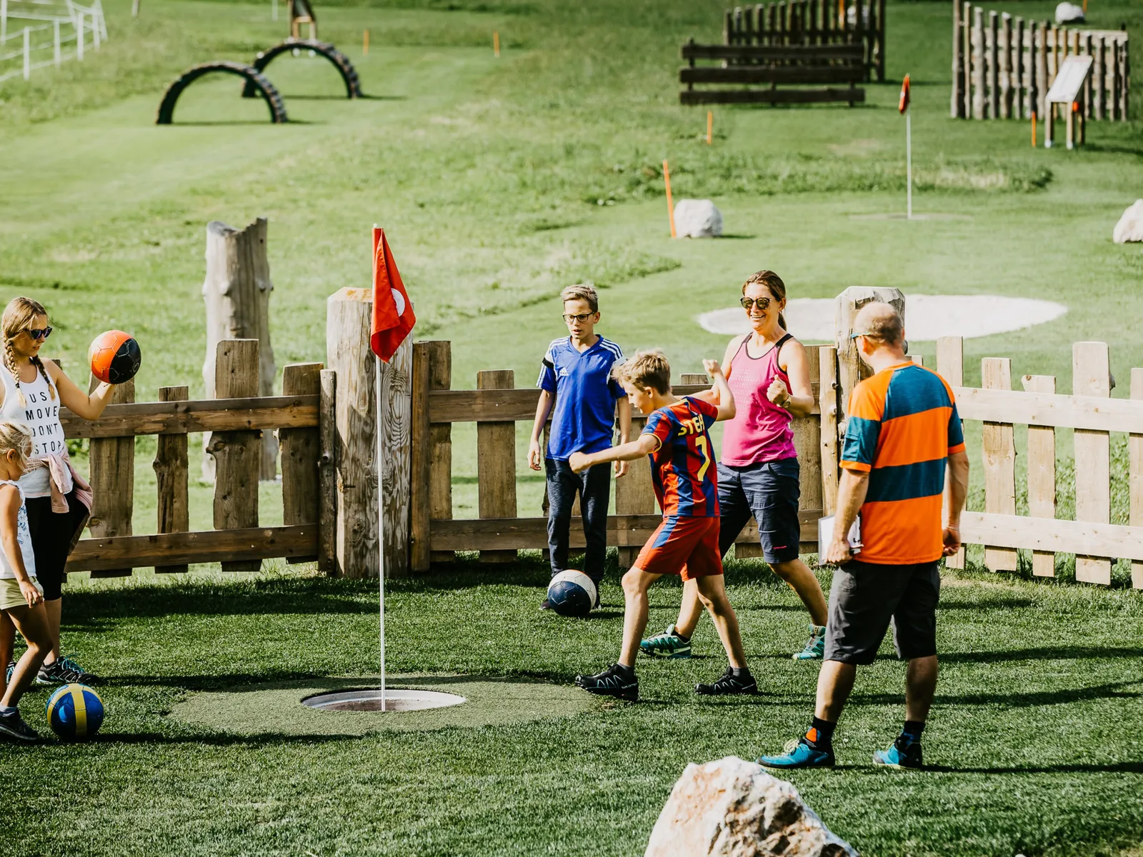 Family playing football golf on a green meadow with obstacles