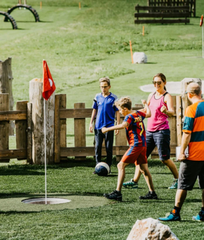 Familie spielt Fußballgolf auf einer grünen Wiese mit Hindernissen