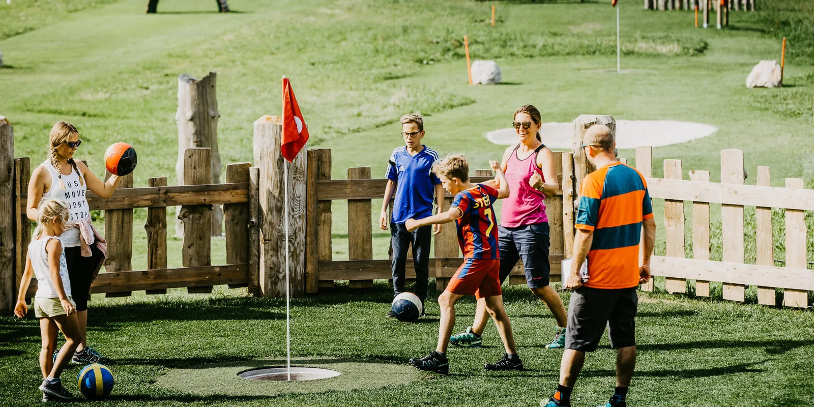 Familie spielt Fußballgolf auf einer grünen Wiese mit Hindernissen
