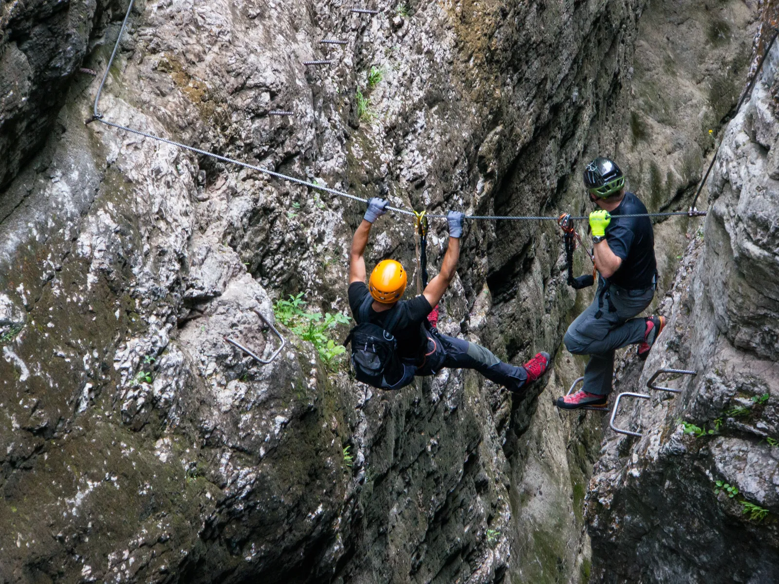 Kletterer am Stahlseil in steiler Felswand, gesichert durch Helm und Klettersteigset