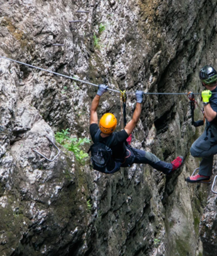 Kletterer am Stahlseil in steiler Felswand, gesichert durch Helm und Klettersteigset