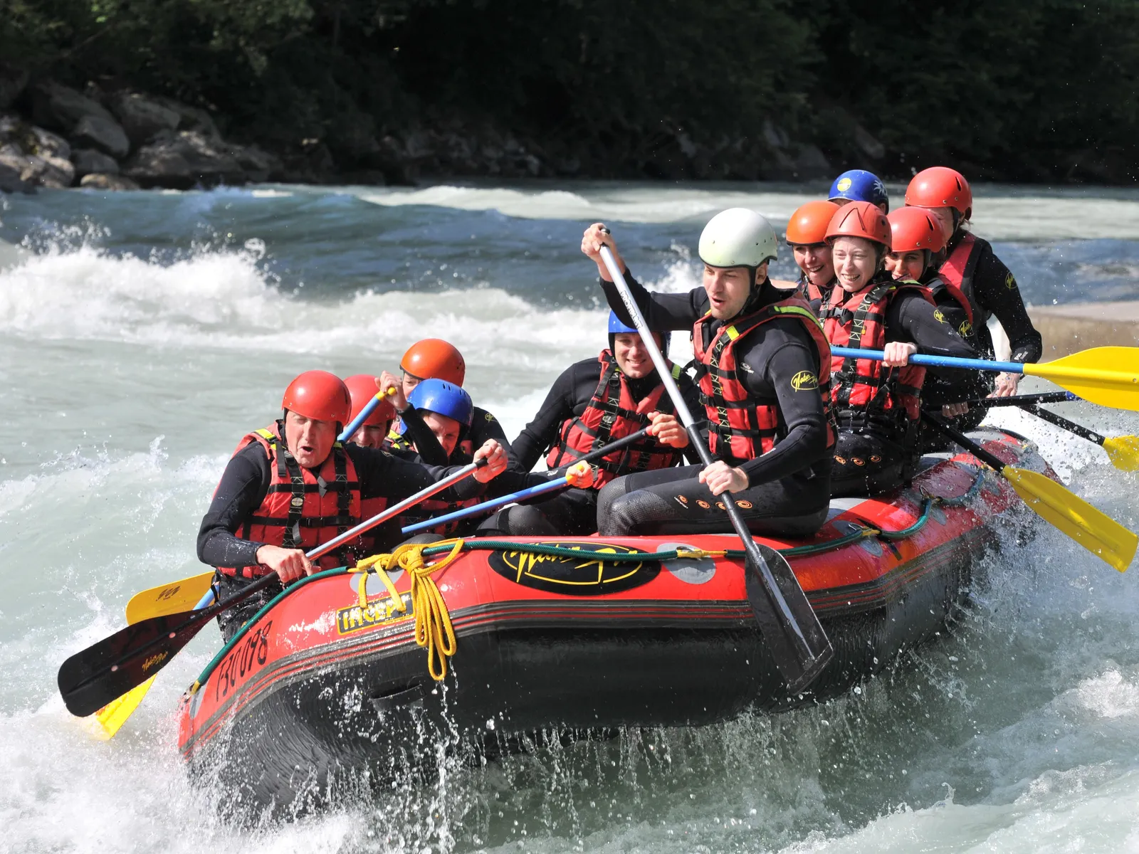 Gruppe im Raftingboot auf reißendem Fluss mit Paddeln und Helmen