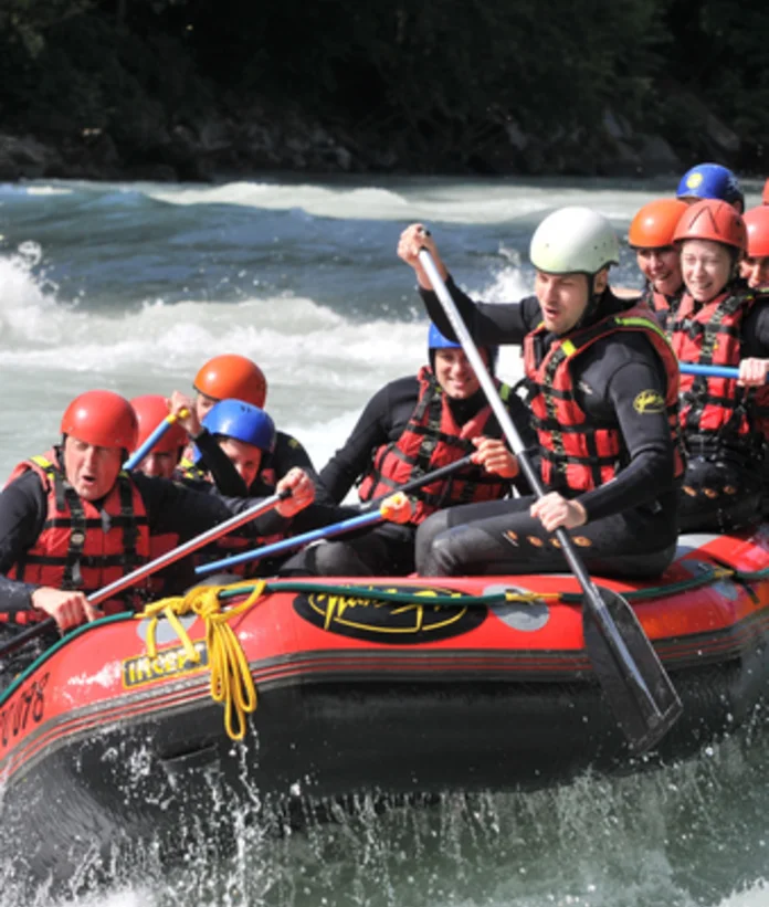 Gruppe im Raftingboot auf reißendem Fluss mit Paddeln und Helmen