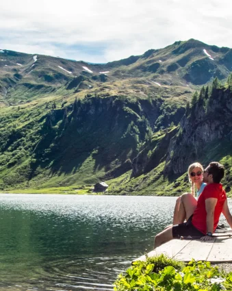 Paar sitzt am Tappenkarsee vor Bergpanorama mit grünen Hängen und schneebedeckten Gipfeln