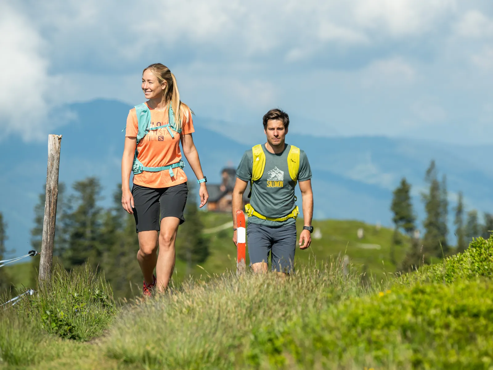 Wanderer auf Bergpfad mit Gras, im Hintergrund Berge und blauer Himmel