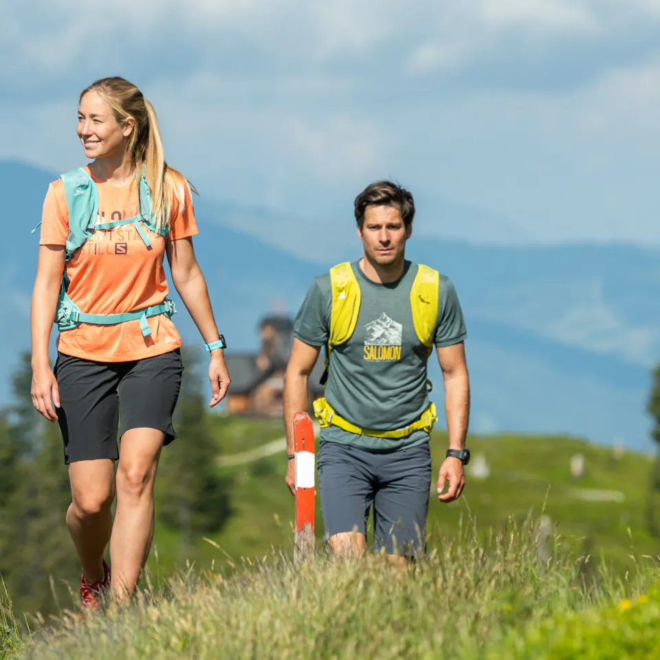 Wanderer auf Bergpfad mit Gras, im Hintergrund Berge und blauer Himmel