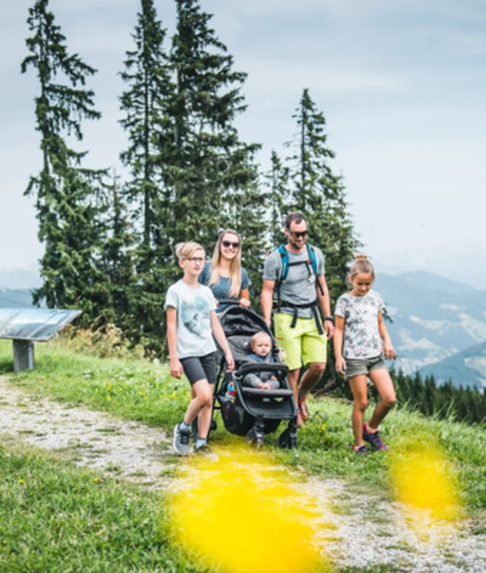 Family with stroller hiking on a green hill with mountain view