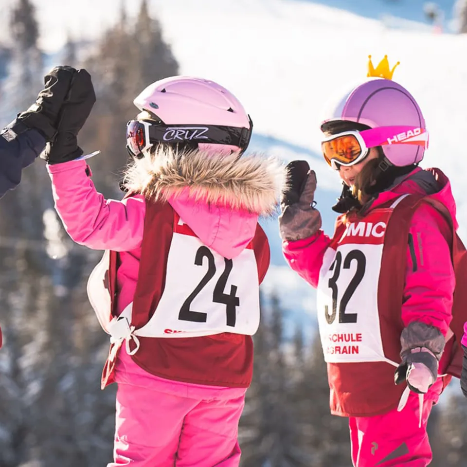 Zwei kleine Mädchen in Skianzügen geben High-Five auf der Skipiste
