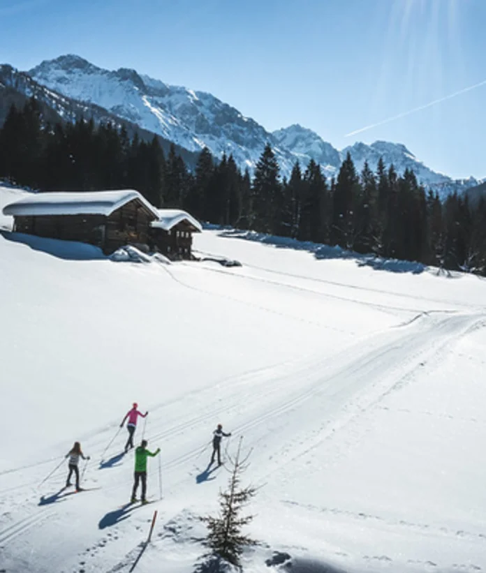 Langläufer auf Loipe vor verschneiter Landschaft mit Hütte und Bergen