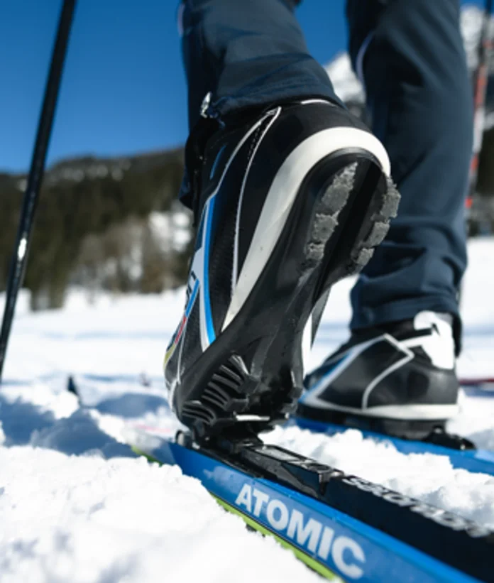 Langlaufschuh auf Ski im Schnee, Stöcke im Hintergrund