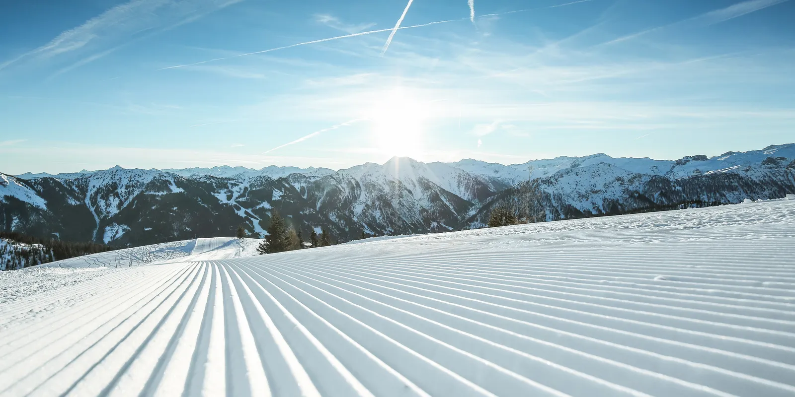 Präparierte Skipiste im Skigebiet Shuttleberg Flachauwinkl-Kleinarl vor Bergpanorama unter blauem Himmel
