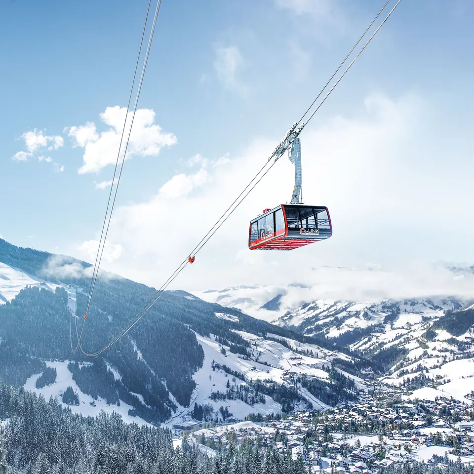 Rote Gondelbahn schwebt über verschneite Berglandschaft mit Ortschaft Wagrain