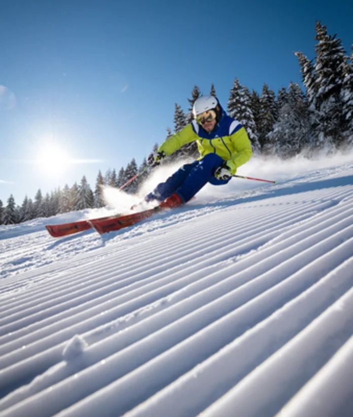 Skier on groomed slope with snow and trees in the background