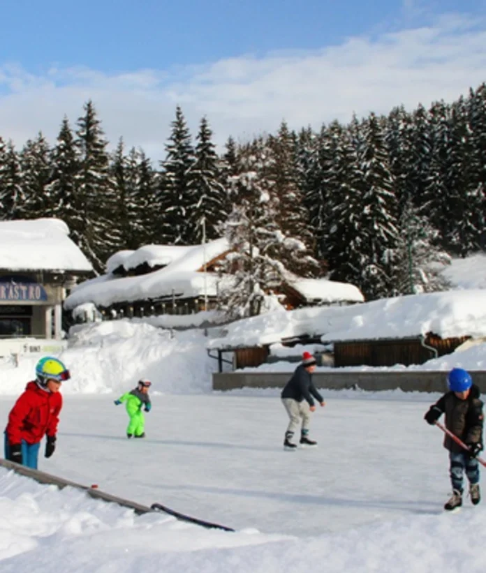 Kinder laufen auf einer Eisfläche vor verschneiten Häusern und Bäumen