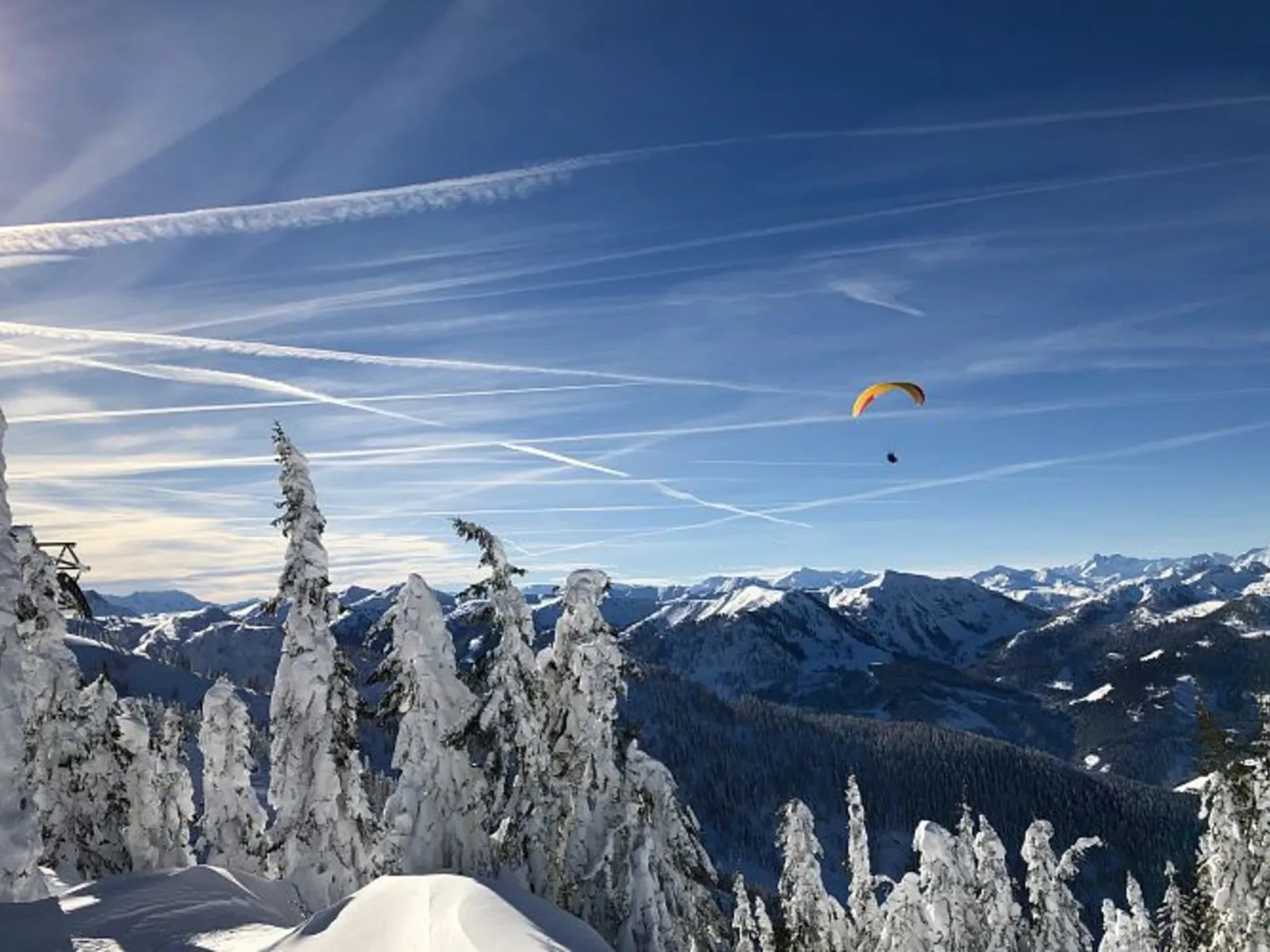 Paragleiter fliegt über verschneite Berge im Winterhimmel von Wagrain-Kleinarl