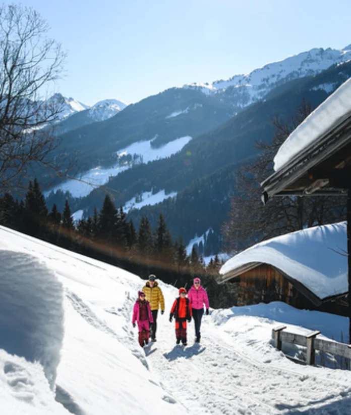 Familie wandert im Winter auf verschneitem Pfad vor Bergkulisse