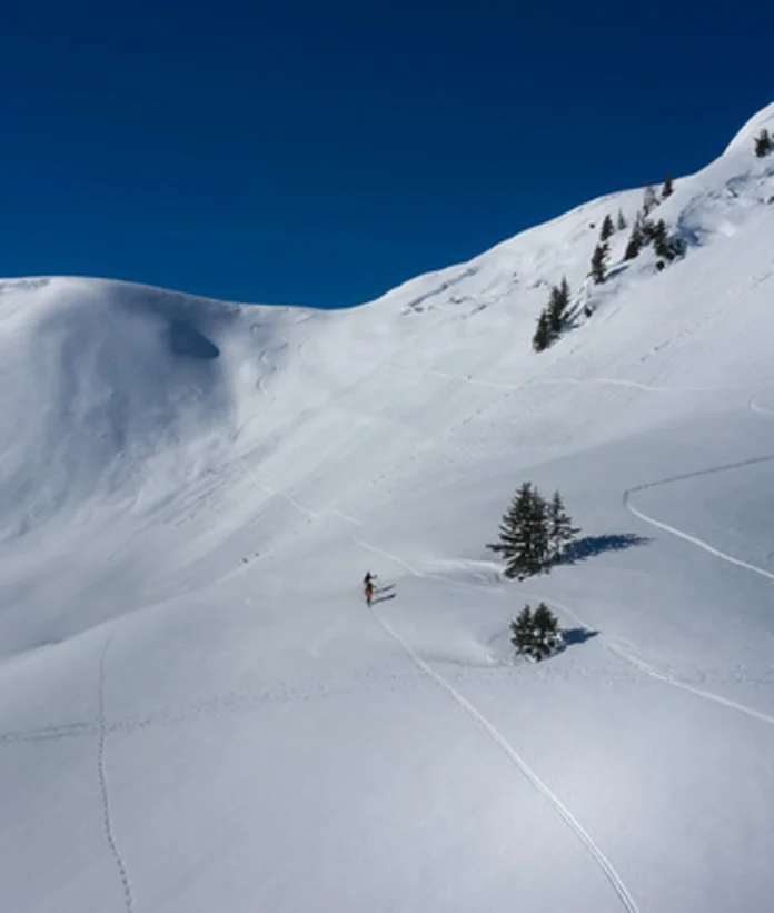 Skitour auf schneebedecktem Berg unter blauem Himmel, Spuren im Schnee sichtbar