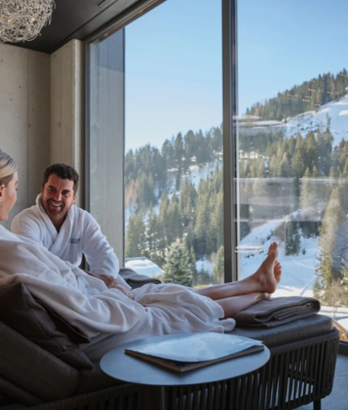 Paar in Bademänteln entspannt mit Bergblick im Wellnessbereich